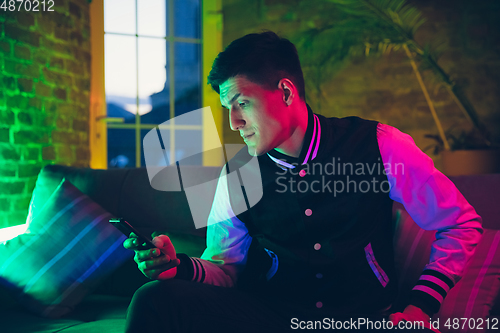 Image of Cinematic portrait of handsome young man using devices, gadgets in neon lighted interior. Youth culture, bright colors