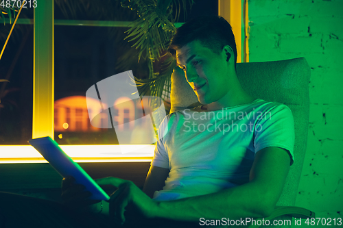 Image of Cinematic portrait of handsome young man using devices, gadgets in neon lighted interior. Youth culture, bright colors