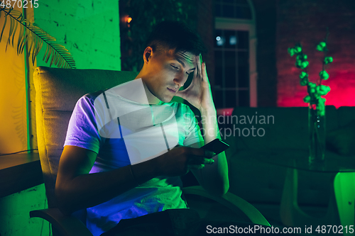 Image of Cinematic portrait of handsome young man using devices, gadgets in neon lighted interior. Youth culture, bright colors