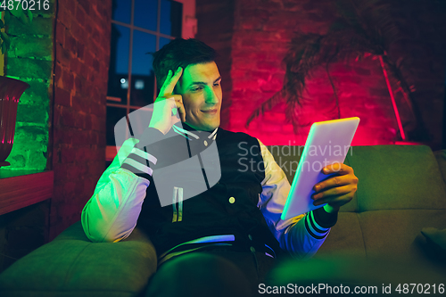 Image of Cinematic portrait of handsome young man using devices, gadgets in neon lighted interior. Youth culture, bright colors