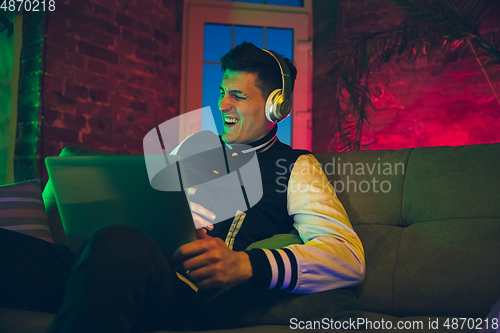 Image of Cinematic portrait of handsome young man using devices, gadgets in neon lighted interior. Youth culture, bright colors