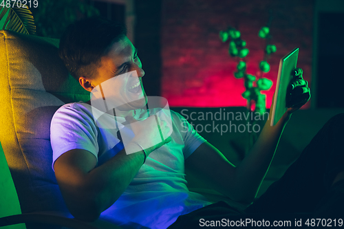 Image of Cinematic portrait of handsome young man using devices, gadgets in neon lighted interior. Youth culture, bright colors