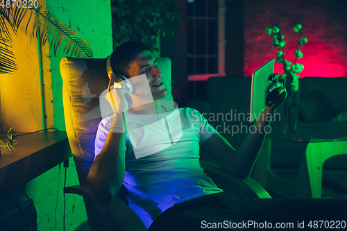 Image of Cinematic portrait of handsome young man using devices, gadgets in neon lighted interior. Youth culture, bright colors