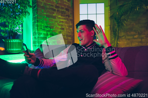 Image of Cinematic portrait of handsome young man using devices, gadgets in neon lighted interior. Youth culture, bright colors