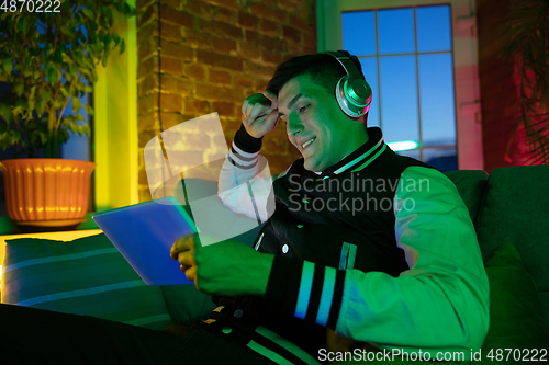 Image of Cinematic portrait of handsome young man using devices, gadgets in neon lighted interior. Youth culture, bright colors