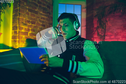 Image of Cinematic portrait of handsome young man using devices, gadgets in neon lighted interior. Youth culture, bright colors