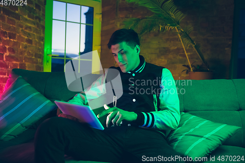 Image of Cinematic portrait of handsome young man using devices, gadgets in neon lighted interior. Youth culture, bright colors