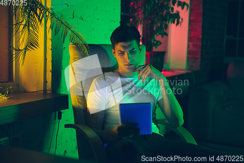 Image of Cinematic portrait of handsome young man using devices, gadgets in neon lighted interior. Youth culture, bright colors