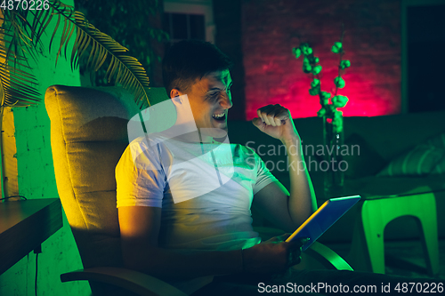 Image of Cinematic portrait of handsome young man using devices, gadgets in neon lighted interior. Youth culture, bright colors