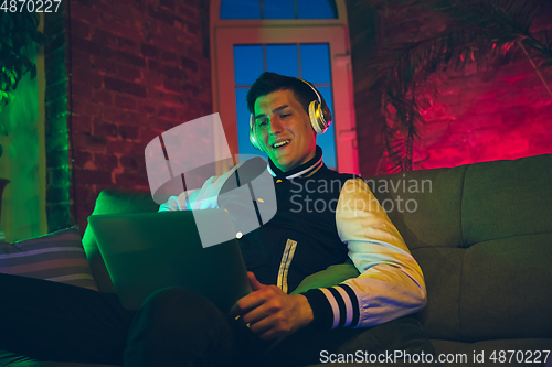 Image of Cinematic portrait of handsome young man using devices, gadgets in neon lighted interior. Youth culture, bright colors