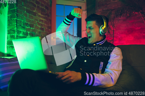 Image of Cinematic portrait of handsome young man using devices, gadgets in neon lighted interior. Youth culture, bright colors