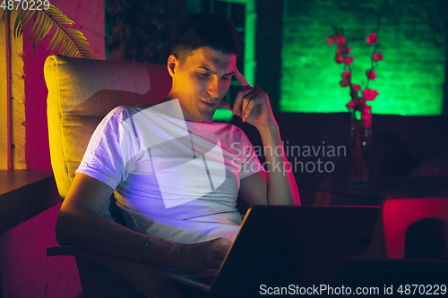 Image of Cinematic portrait of handsome young man using devices, gadgets in neon lighted interior. Youth culture, bright colors