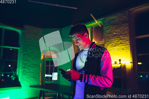 Image of Cinematic portrait of handsome young man using devices, gadgets in neon lighted interior. Youth culture, bright colors