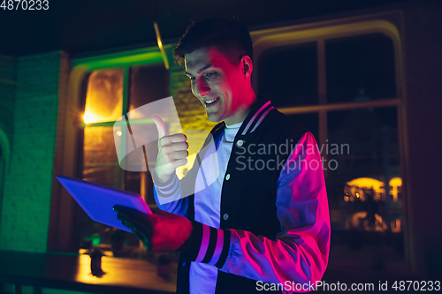 Image of Cinematic portrait of handsome young man using devices, gadgets in neon lighted interior. Youth culture, bright colors