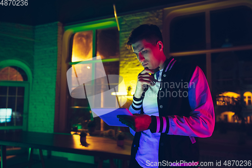 Image of Cinematic portrait of handsome young man using devices, gadgets in neon lighted interior. Youth culture, bright colors