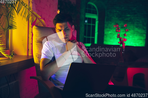 Image of Cinematic portrait of handsome young man using devices, gadgets in neon lighted interior. Youth culture, bright colors