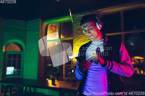 Image of Cinematic portrait of handsome young man using devices, gadgets in neon lighted interior. Youth culture, bright colors