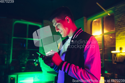 Image of Cinematic portrait of handsome young man using devices, gadgets in neon lighted interior. Youth culture, bright colors