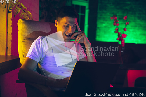 Image of Cinematic portrait of handsome young man using devices, gadgets in neon lighted interior. Youth culture, bright colors