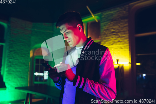 Image of Cinematic portrait of handsome young man using devices, gadgets in neon lighted interior. Youth culture, bright colors