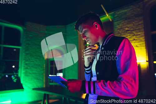 Image of Cinematic portrait of handsome young man using devices, gadgets in neon lighted interior. Youth culture, bright colors