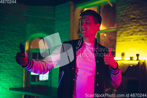 Image of Cinematic portrait of handsome young man using devices, gadgets in neon lighted interior. Youth culture, bright colors