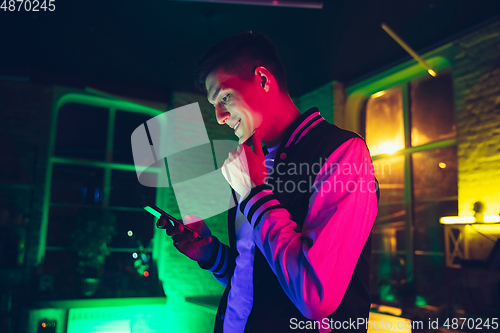 Image of Cinematic portrait of handsome young man using devices, gadgets in neon lighted interior. Youth culture, bright colors