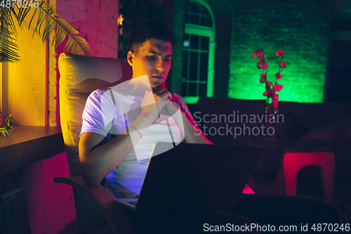 Image of Cinematic portrait of handsome young man using devices, gadgets in neon lighted interior. Youth culture, bright colors