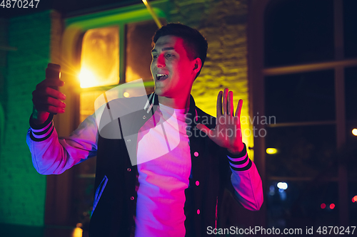 Image of Cinematic portrait of handsome young man using devices, gadgets in neon lighted interior. Youth culture, bright colors