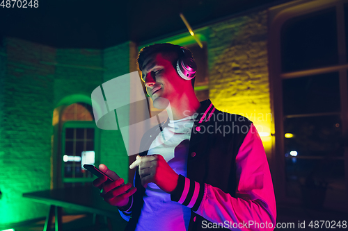 Image of Cinematic portrait of handsome young man using devices, gadgets in neon lighted interior. Youth culture, bright colors