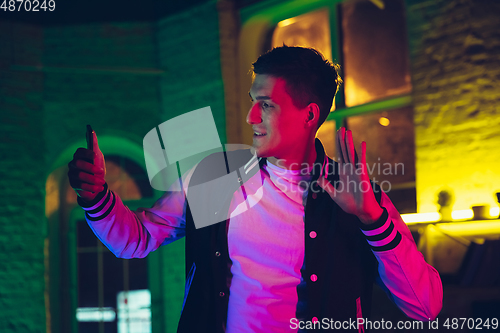 Image of Cinematic portrait of handsome young man using devices, gadgets in neon lighted interior. Youth culture, bright colors