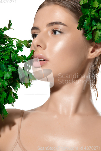 Image of Vitamins. Close up of beautiful young woman with green leaves on her face over white background. Cosmetics and makeup, natural and eco treatment, skin care