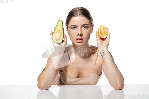 Image of Choice. Beautiful young woman with fresh avocado and orange pieces over white background. Cosmetics and makeup, natural and eco treatment, skin care.