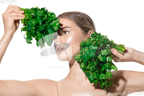 Image of Vitamins. Close up of beautiful young woman with green leaves on her face over white background. Cosmetics and makeup, natural and eco treatment, skin care