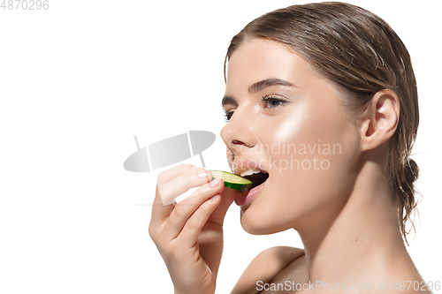 Image of Nature way. Beautiful young woman biting fresh cucumber over white background. Cosmetics and makeup, natural and eco treatment, skin care.