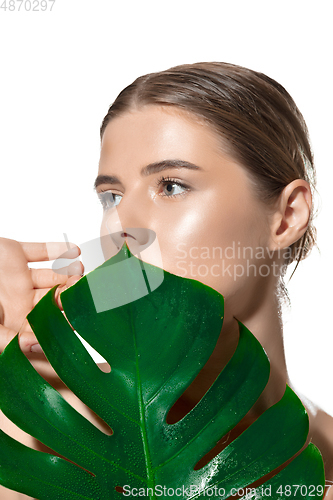 Image of Inspiration. Close up of beautiful young woman with green leaves on her face over white background. Cosmetics and makeup, natural and eco treatment, skin care