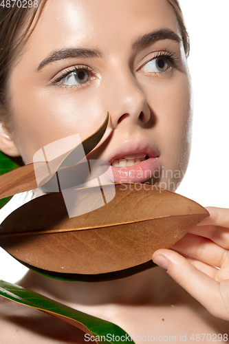 Image of Lovely. Close up of beautiful young woman with green leaves on her face over white background. Cosmetics and makeup, natural and eco treatment, skin care