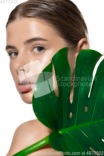 Image of Youth. Close up of beautiful young woman with green leaves on her face over white background. Cosmetics and makeup, natural and eco treatment, skin care