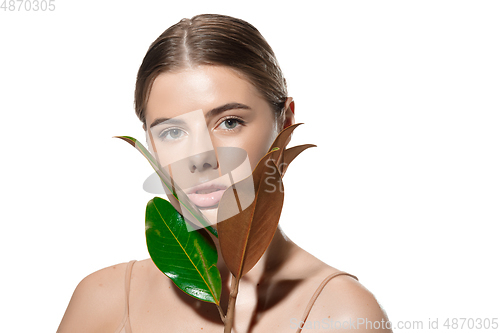 Image of Protection. Beautiful young woman with green leaves on her face over white background. Cosmetics and makeup, natural and eco treatment, skin care