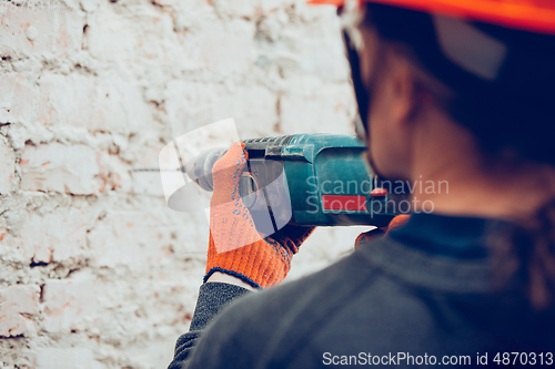 Image of Close up of hands of repairman, professional builder working indoors, drills a wall