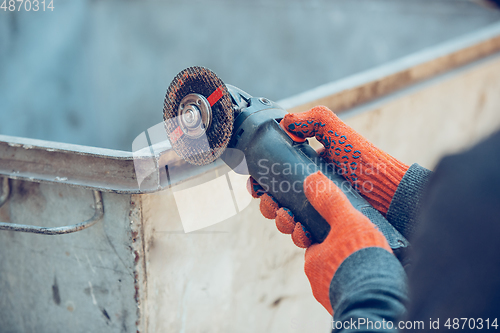 Image of Close up of hands of repairman, professional builder working outdoors, cuts grinder