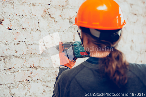 Image of Close up of hands of repairman, professional builder working indoors, drills a wall