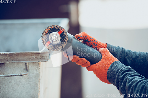 Image of Close up of hands of repairman, professional builder working outdoors, cuts grinder