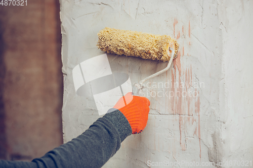 Image of Close up of hands of repairman, professional builder working indoors, coloring the wall