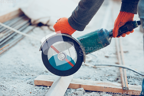 Image of Close up of hands of repairman, professional builder working outdoors, cuts grinder