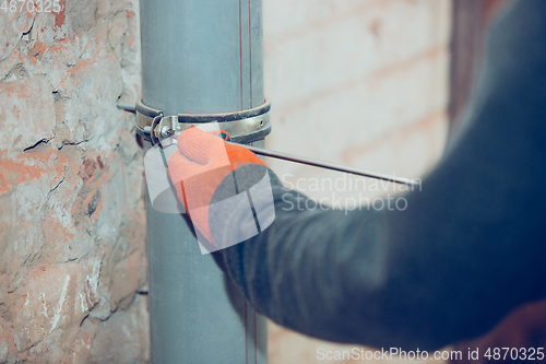 Image of Close up of hands of repairman, professional builder working indoors, installs sewer, duct