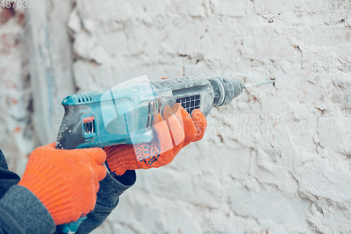 Image of Close up of hands of repairman, professional builder working indoors, drills a wall