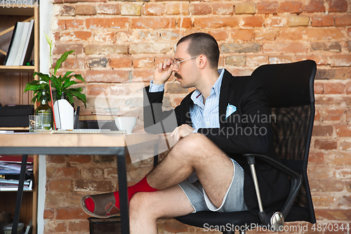 Image of Young man without pants but in jacket working on a computer, laptop. Remote office during coronavirus, fun and comfortable work in underpants