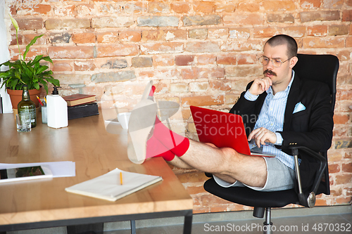 Image of Young man without pants but in jacket working on a computer, laptop. Remote office during coronavirus, fun and comfortable work in underpants