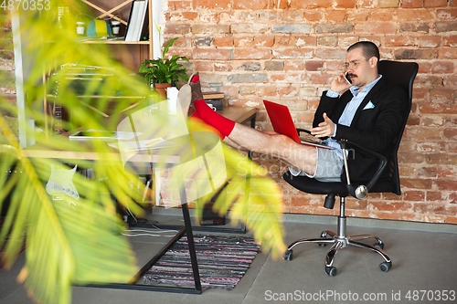 Image of Young man without pants but in jacket working on a computer, laptop. Remote office during coronavirus, fun and comfortable work in underpants